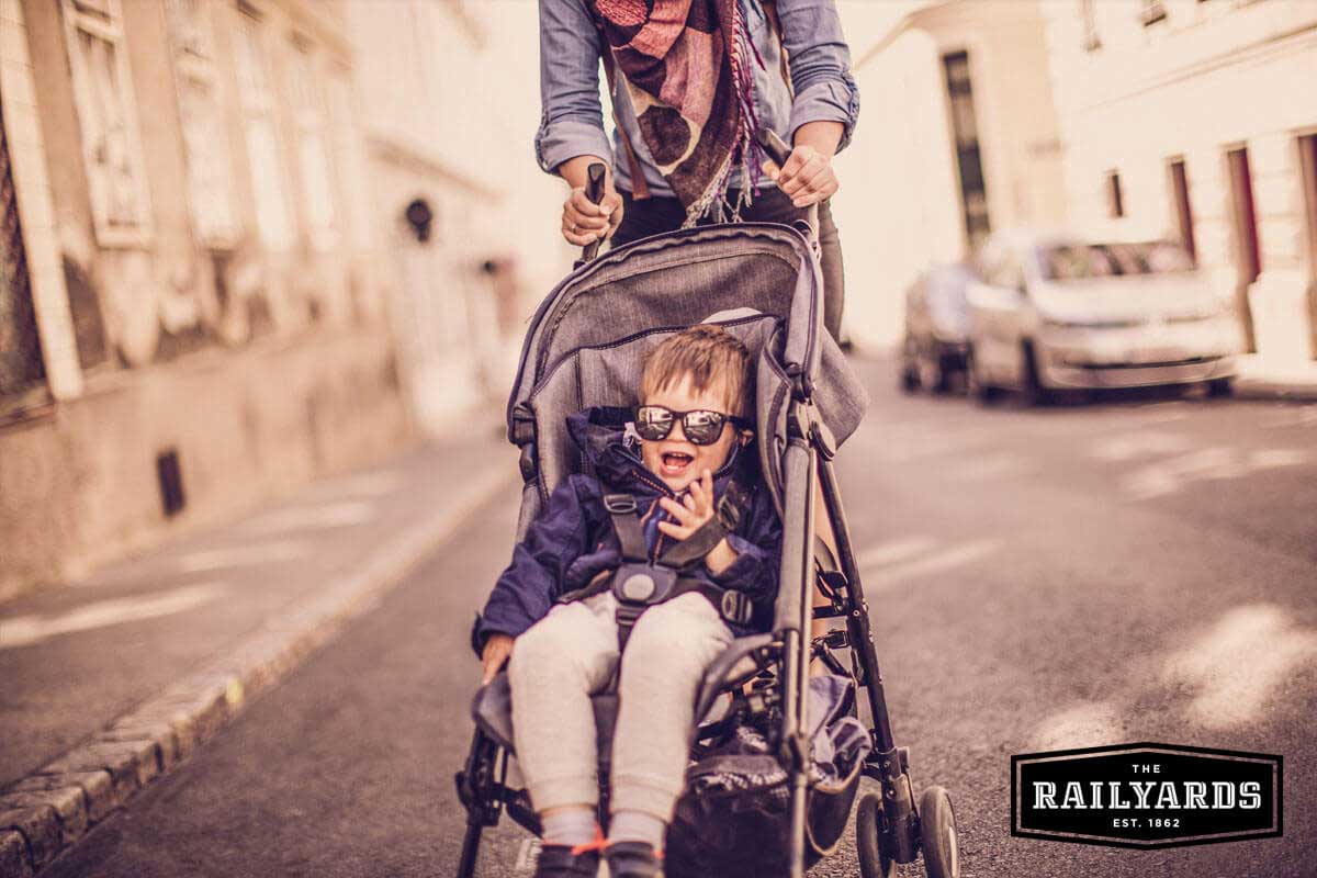 Image of a mom pushing her toddler in a stroller down a city street.