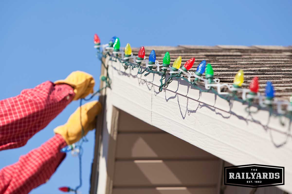 A person hanging Christmas lights on their roof in the winter.