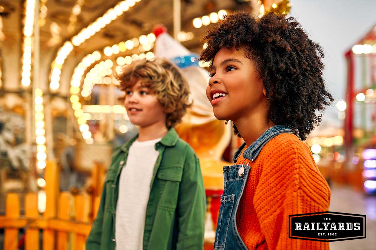 Two children, a young Black girl and young white boy, are in front of a carousel at a State Fair. Discover 10 Summertime activities in Sacramento.