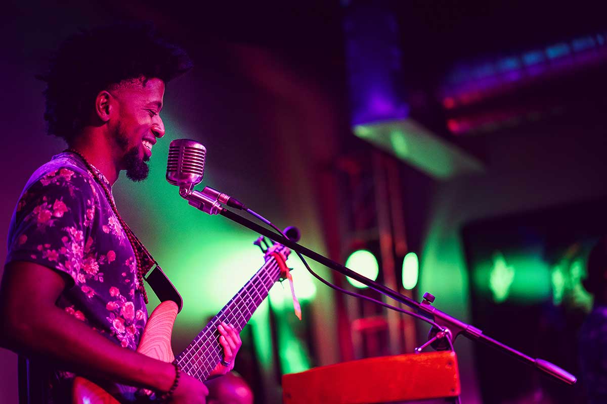 A guitarist is playing in an industrial building lit by green and pink lighting.